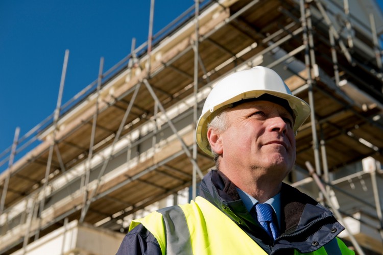 Man in shirt and tie with high vis and hard hat in front of scaffolding