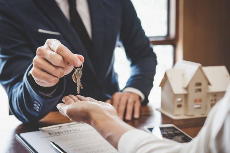 Man in suit handing keys to someone over a desk
