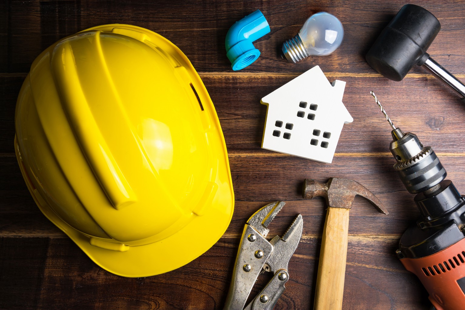 Hard hat, light bulb, wooden house and tools on a wooden background