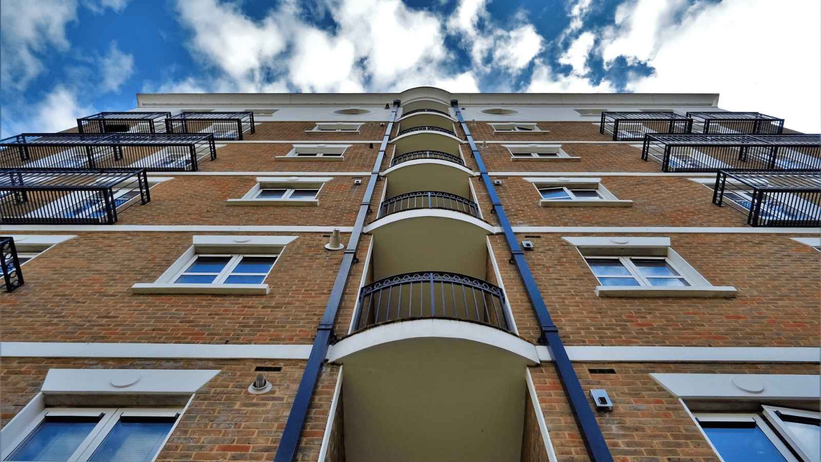 Looking up at a block of flats with blue sky and white clouds